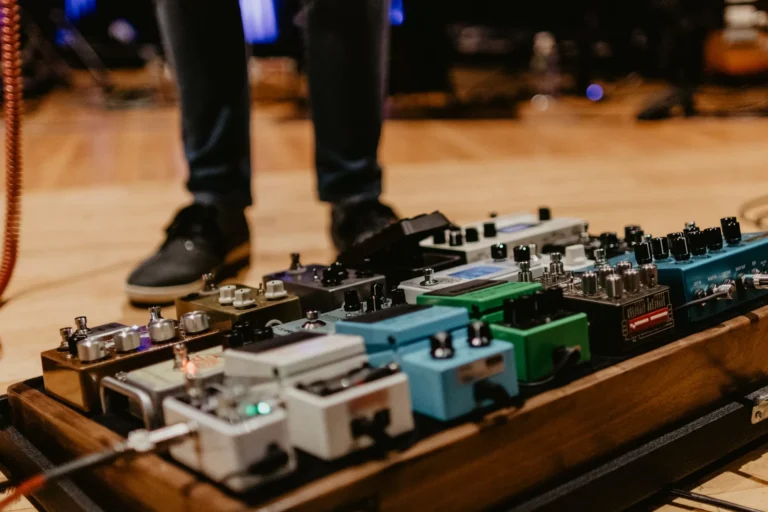 Guitar effects pedalboard on a wooden stage floor with a player standing behind it