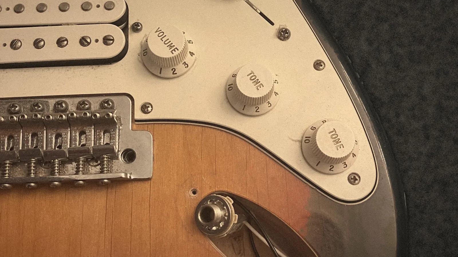 Close-up of a sunburst electric guitar on a repair bench, with the jack plate off and its wiring showing.